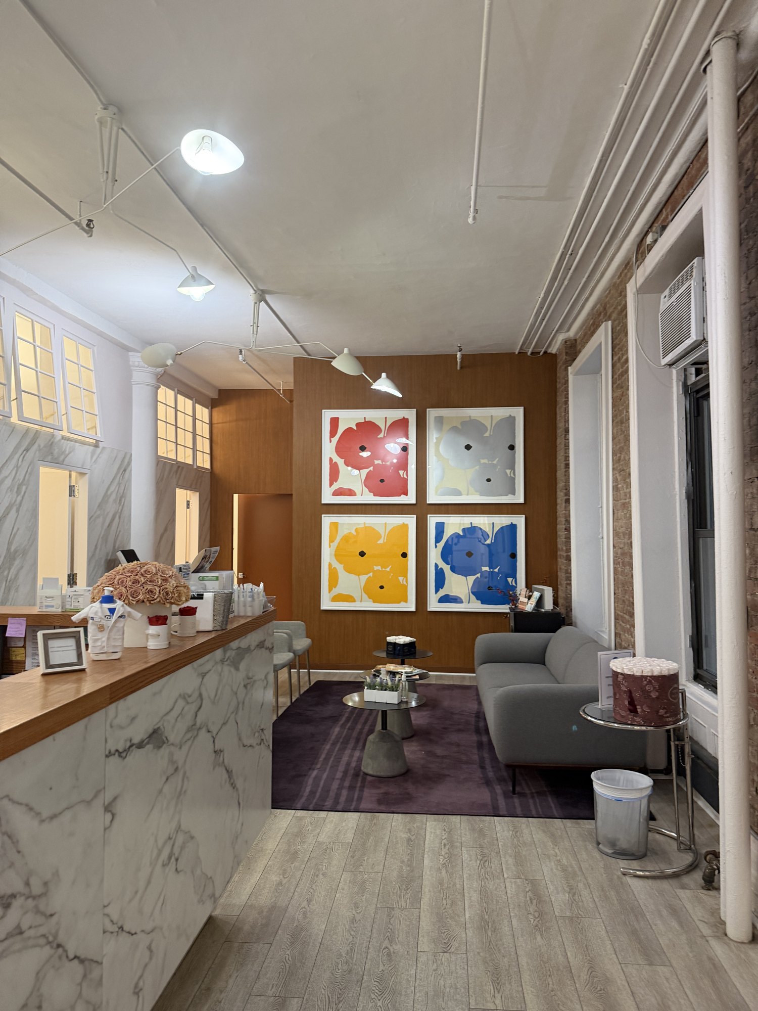 Marble reception desk at Soho DermCare with a four-panel poppy print gallery wall beyond